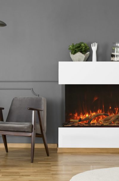Grey armchair between fireplace and cabinet with lamp in flat interior with plant. Real photo